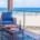 Oceanfront balcony with blue-cushioned wicker seating, wine, and snacks overlooking a sandy beach and surf.