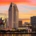 Downtown San Diego skyline above the bay beneath orange and pink sunset clouds, with waterfront lights reflected in the water.
