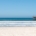 Sandy beach with rolling ocean waves and a wooden pier beneath a clear blue sky.