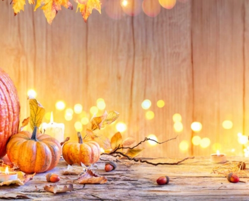 Orange pumpkins, autumn leaves, acorns and glowing candles on a rustic wooden table with a glass lantern.