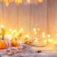 Orange pumpkins, autumn leaves, acorns and glowing candles on a rustic wooden table with a glass lantern.